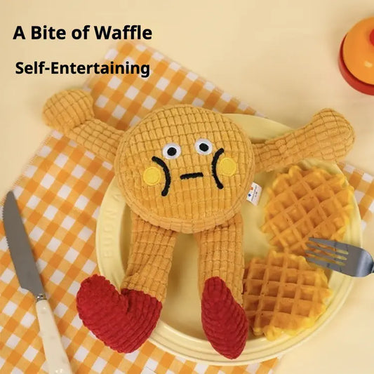 Plush toy resembling a waffle with a face on a checkered tablecloth, accompanied by a knife and waffle iron.